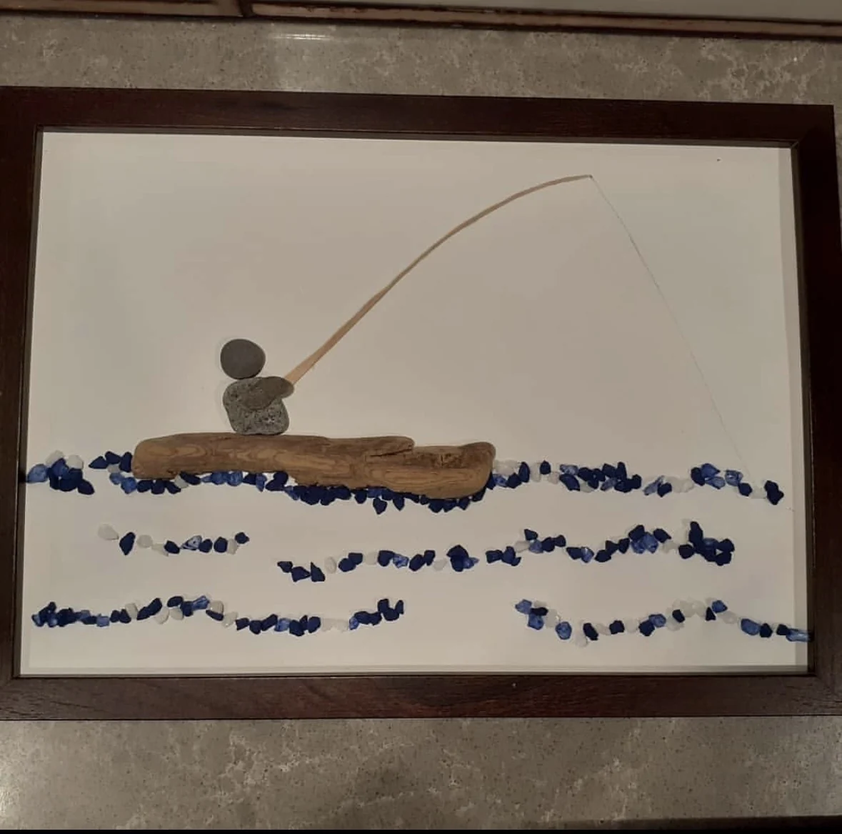 Fishing scene pebble art with driftwood and blue water details