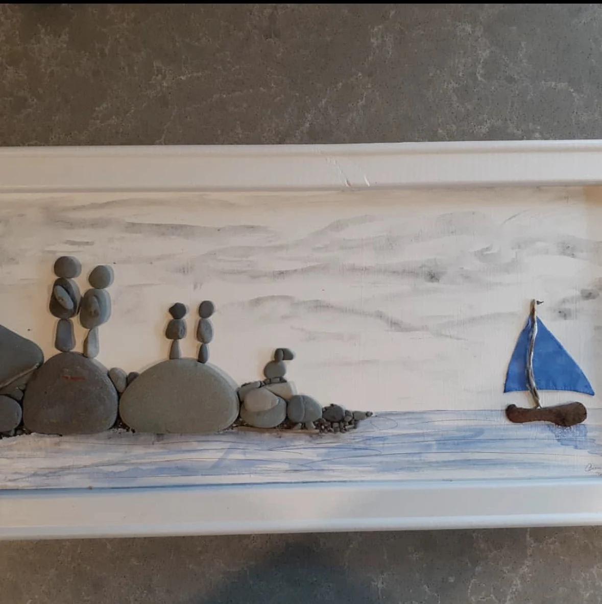 Family pebble figures overlooking a sailboat on the water