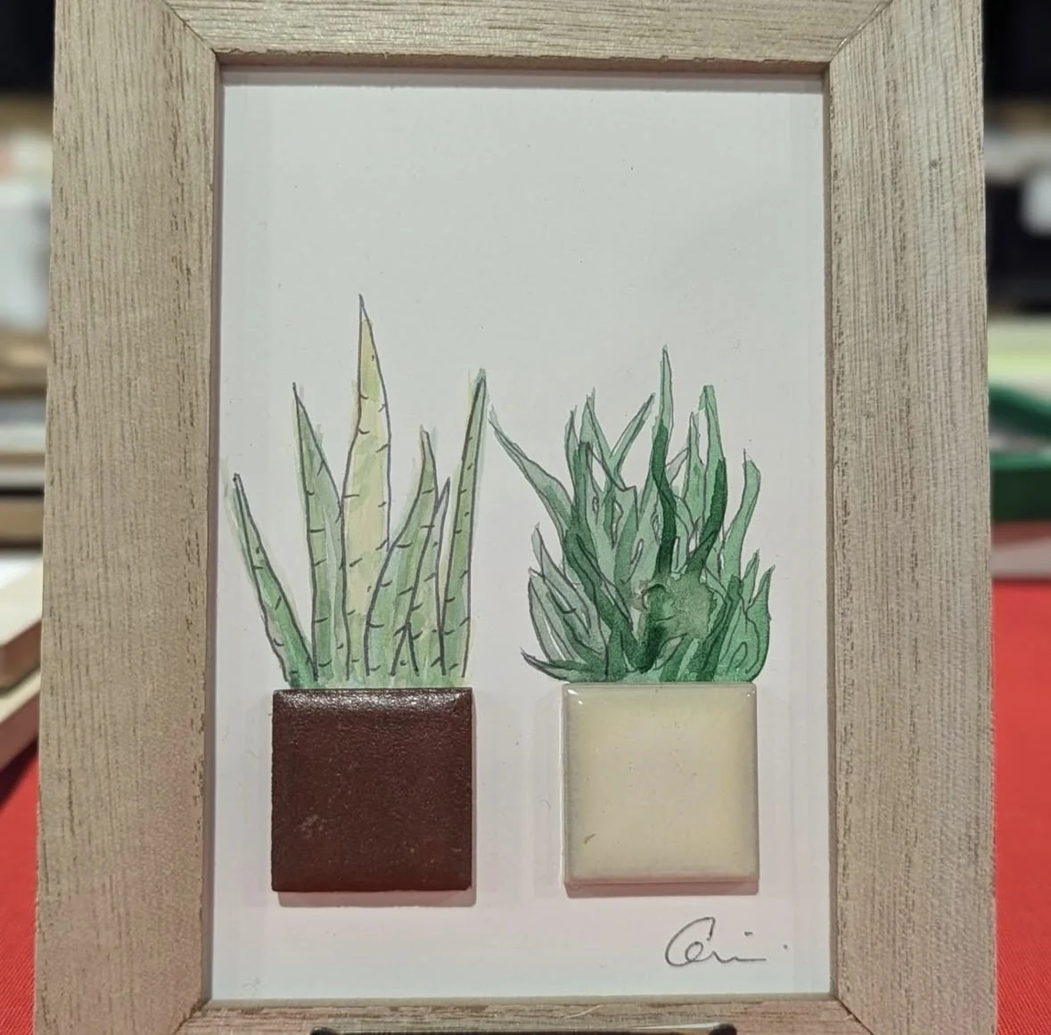 Framed greenery artwork combining painted plants and small tiles